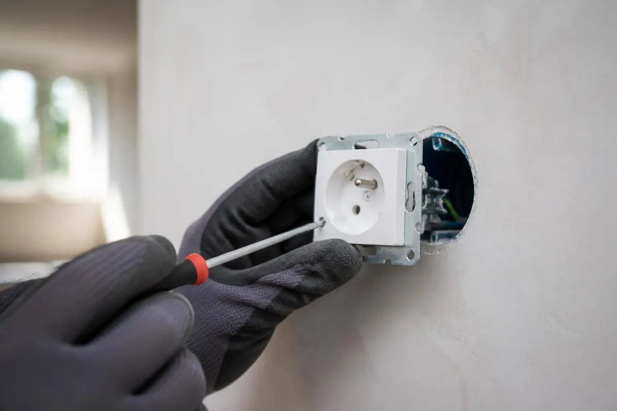 Électricien posant une prise électrique encastrée dans un mur