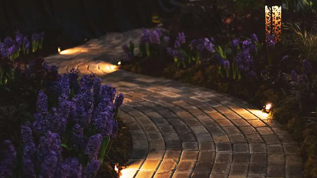 Allée de jardin pavée éclairée par des spots encastrés au sol la nuit, avec borne lumineuse